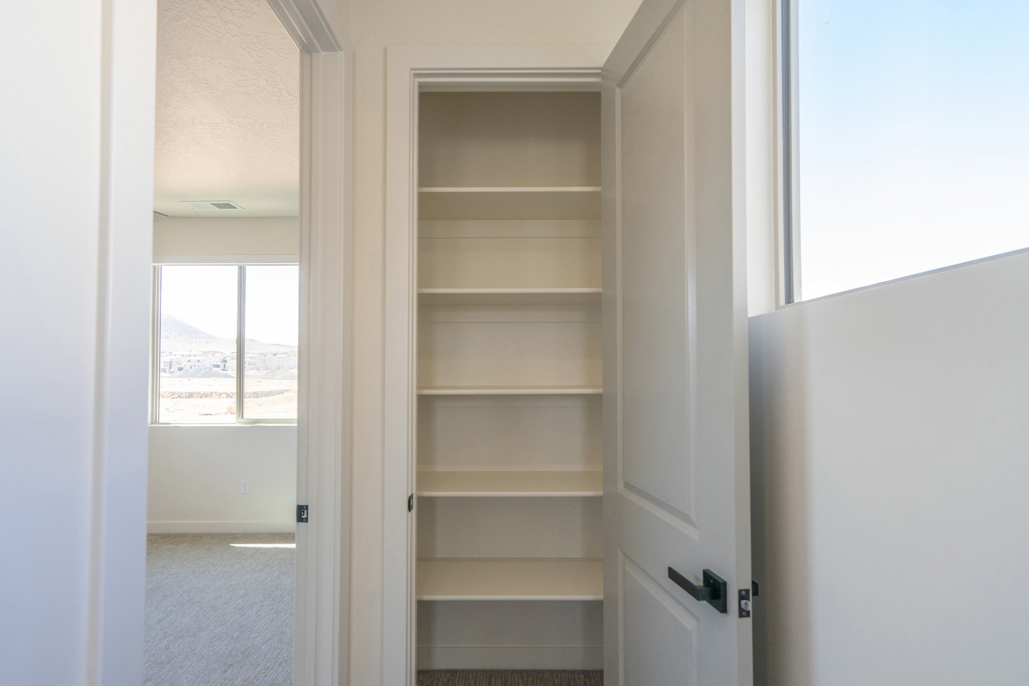 Built-in shelving unit with white finishes and a durable black door handle, positioned opposite a large window offering mountain scenery
