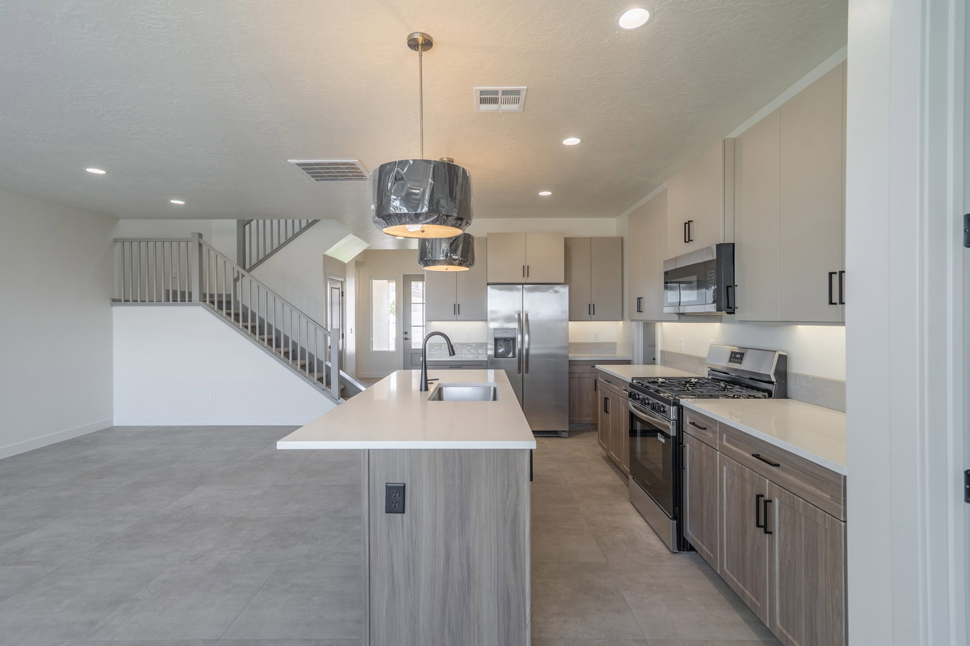 Modern kitchen featuring an island with an undermount sink, light-toned countertops, stainless steel appliances, and two-tone cabinetry