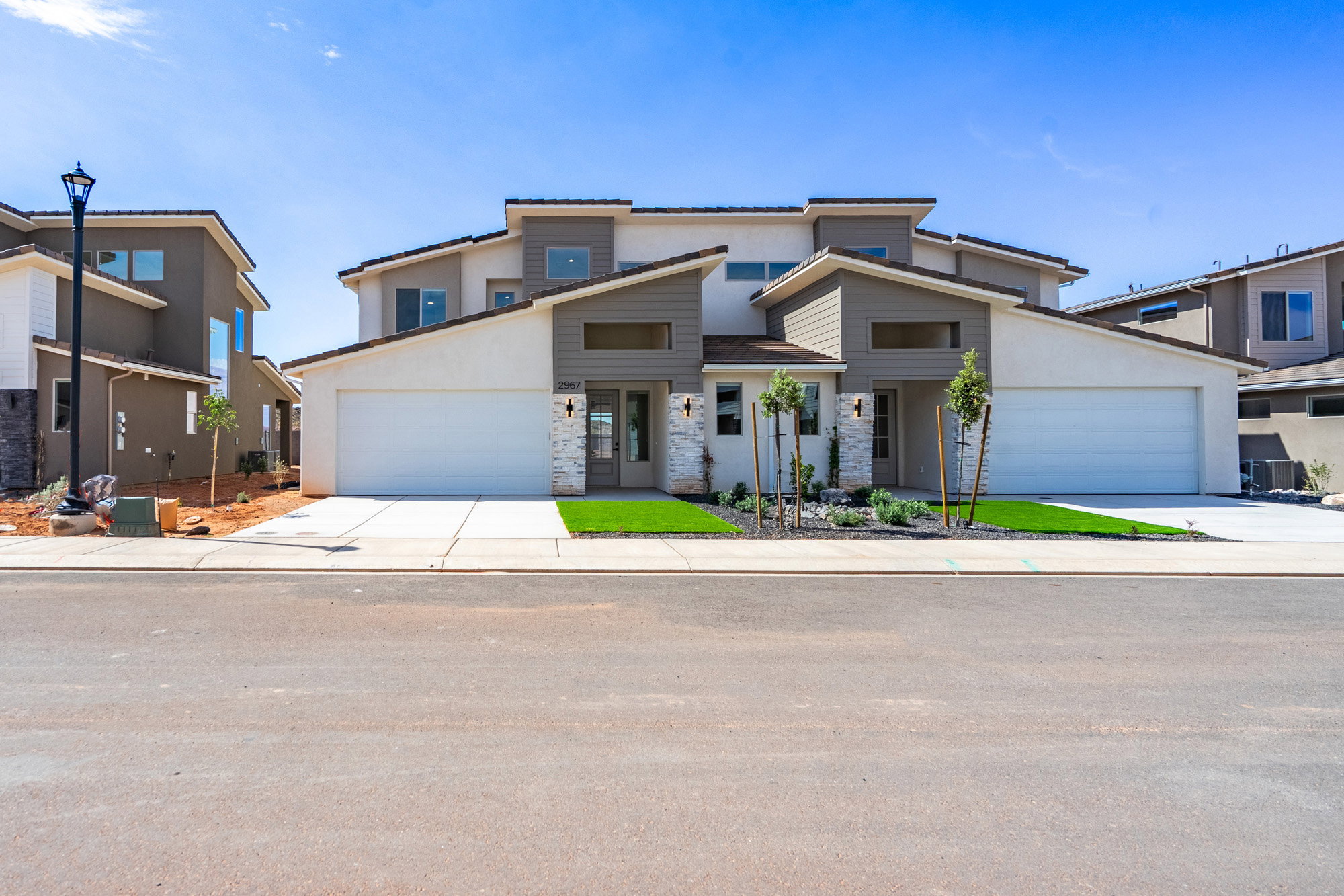 Contemporary duplex featuring a stucco and stone facade, integrated two-car garages, and an artificial turf lawn