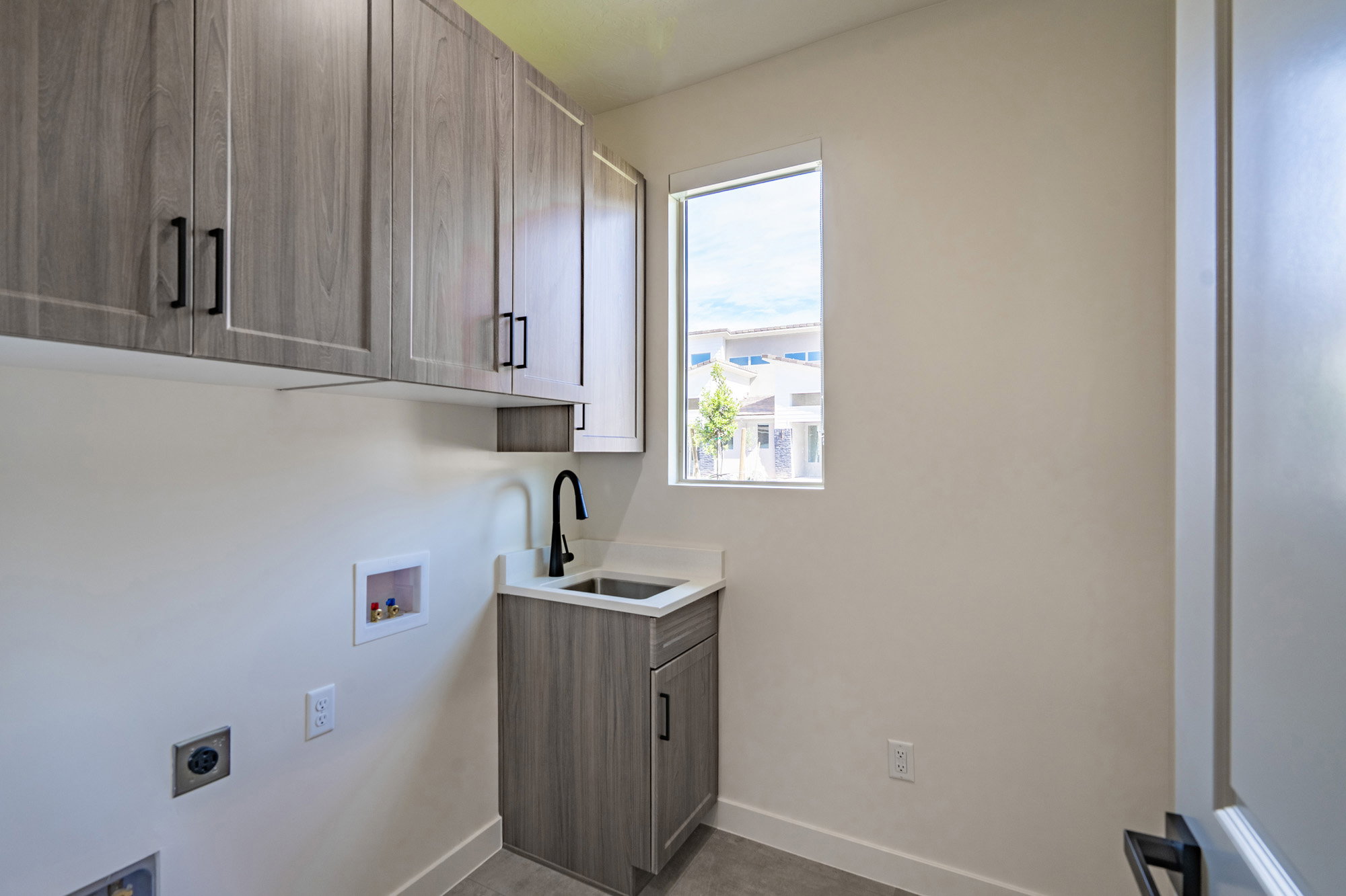 Laundry area featuring wood-finish cabinetry with black hardware, a built-in utility sink with a black faucet, and a window providing natural light