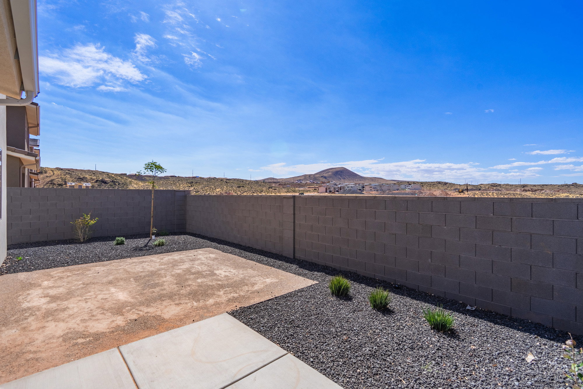 Private backyard featuring a concrete patio, landscaped with dark gravel, and bordered by a block wall