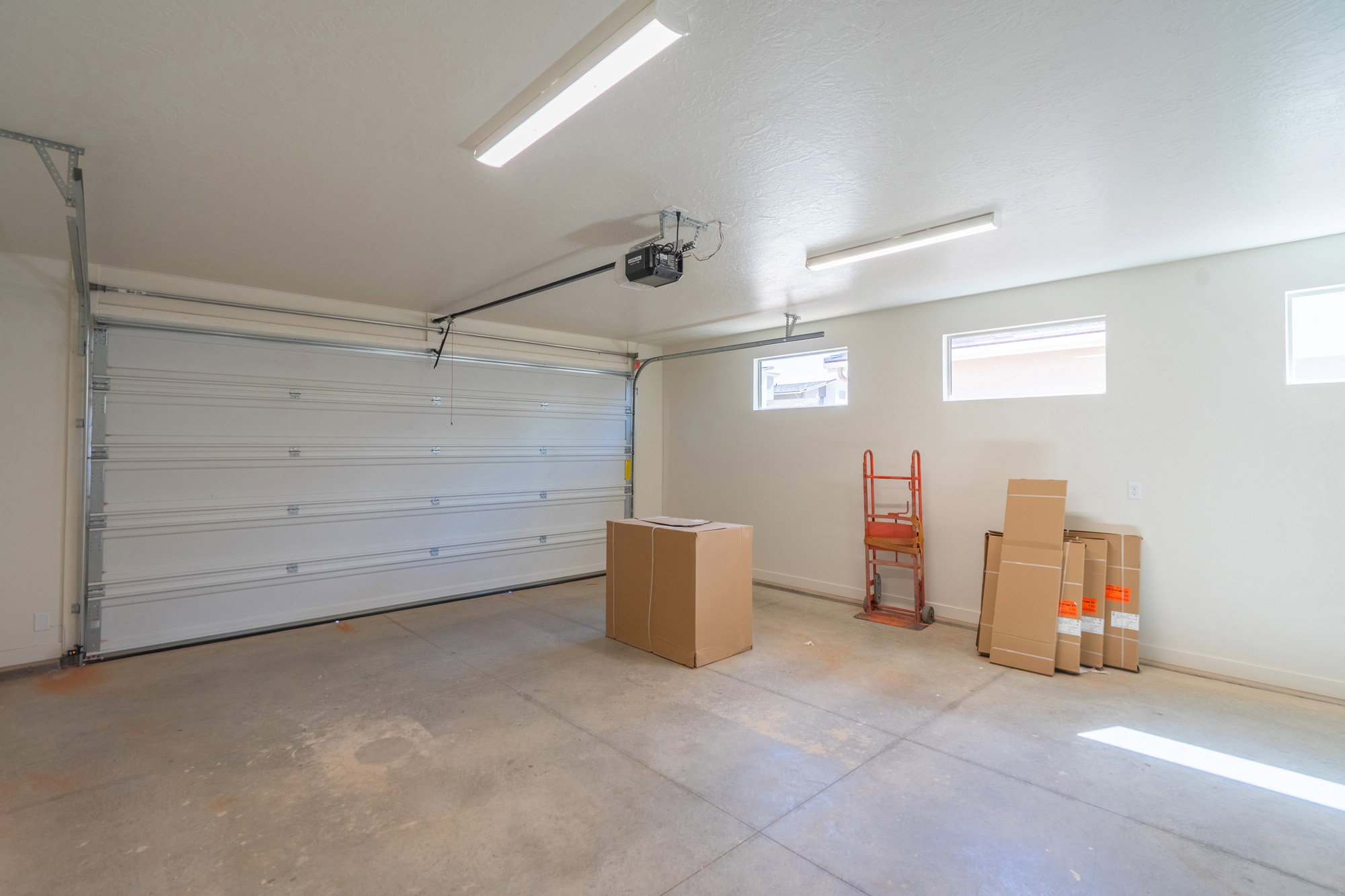 Spacious garage featuring a sectional overhead door, automatic opener, concrete flooring, and multiple high-set windows providing natural light