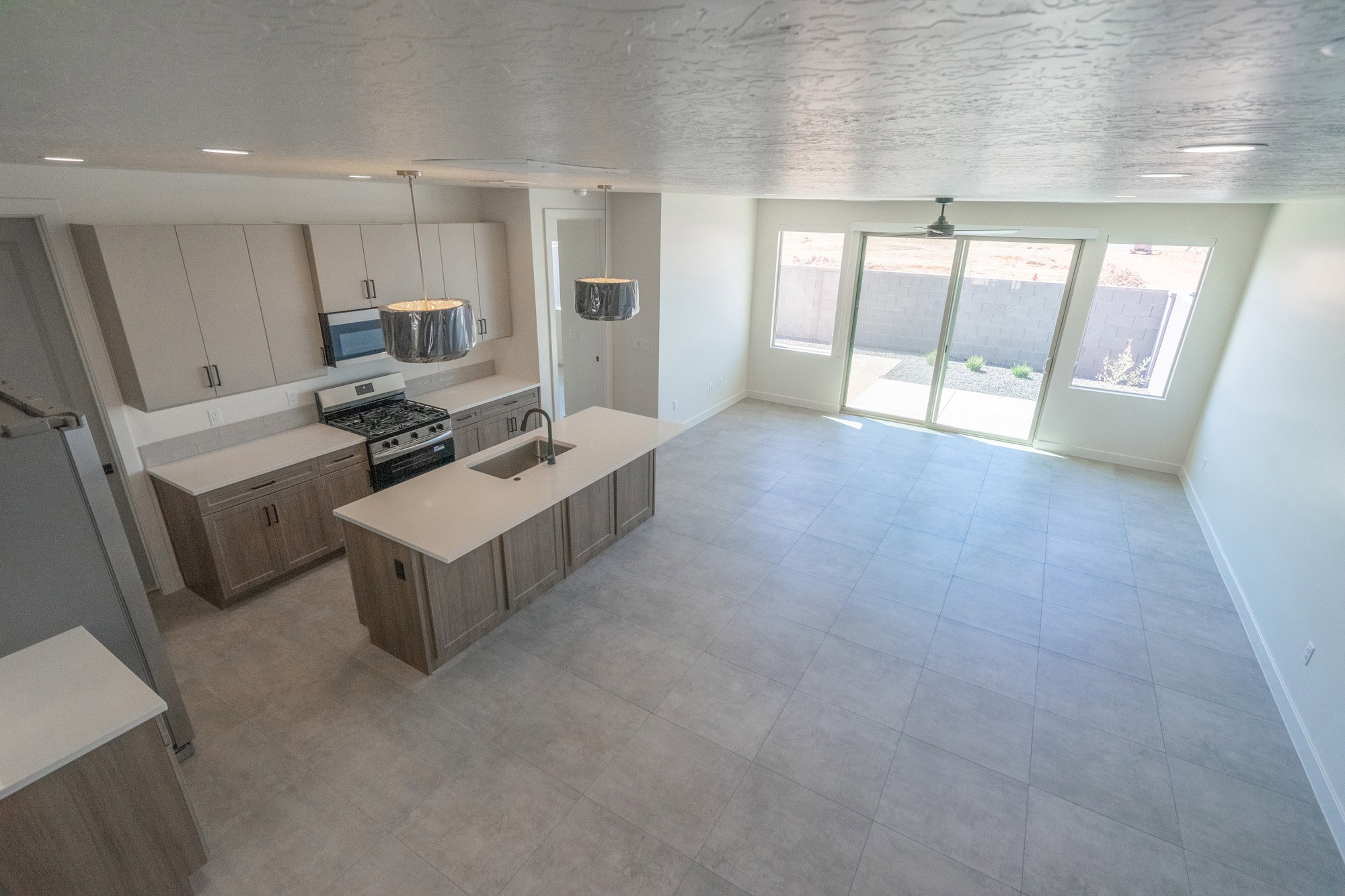 Modern kitchen and living area featuring a central island, stainless steel appliances, pendant lighting, and large format tile flooring