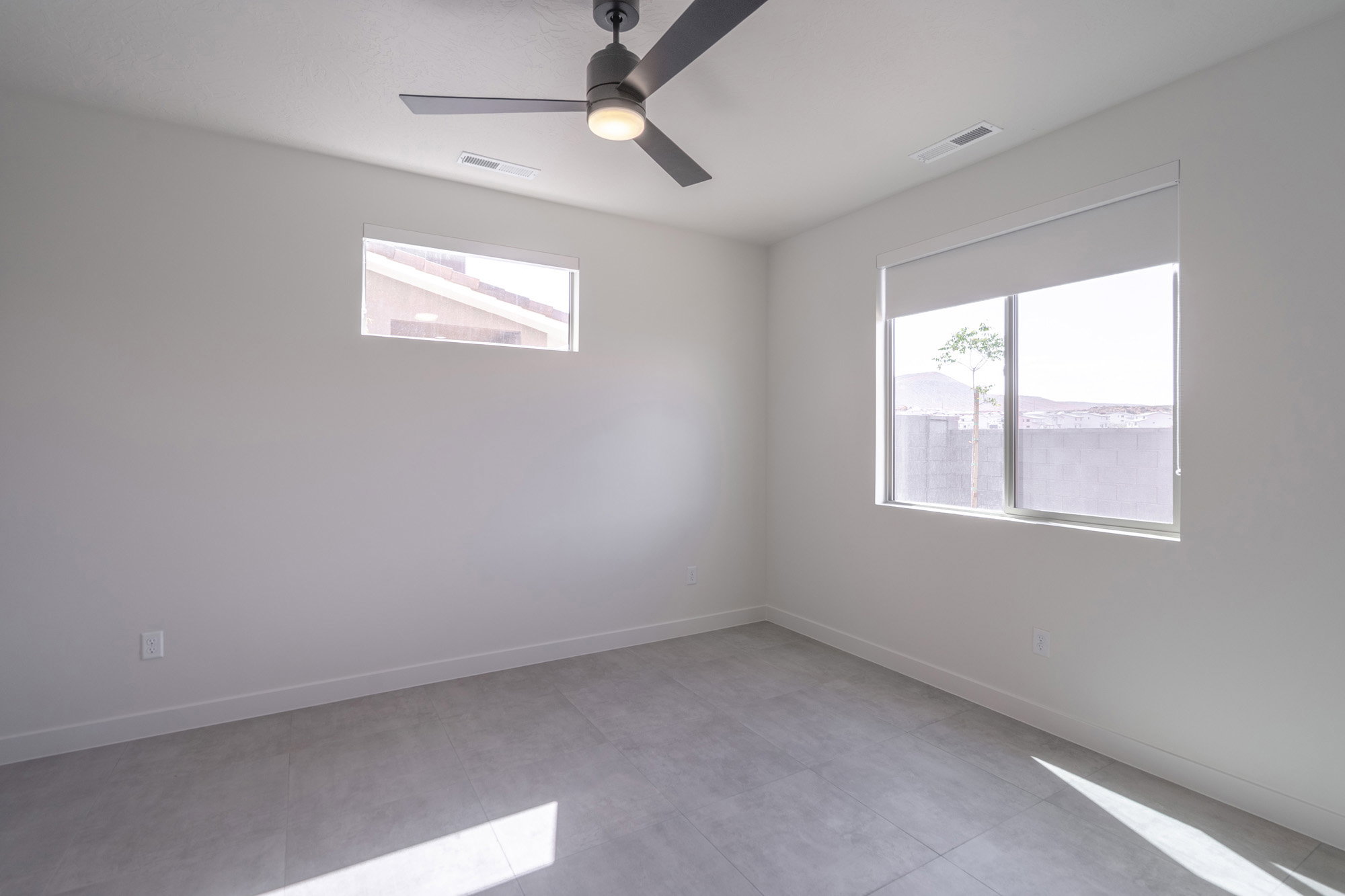 Spacious room featuring a modern ceiling fan, two windows, and light gray tile flooring