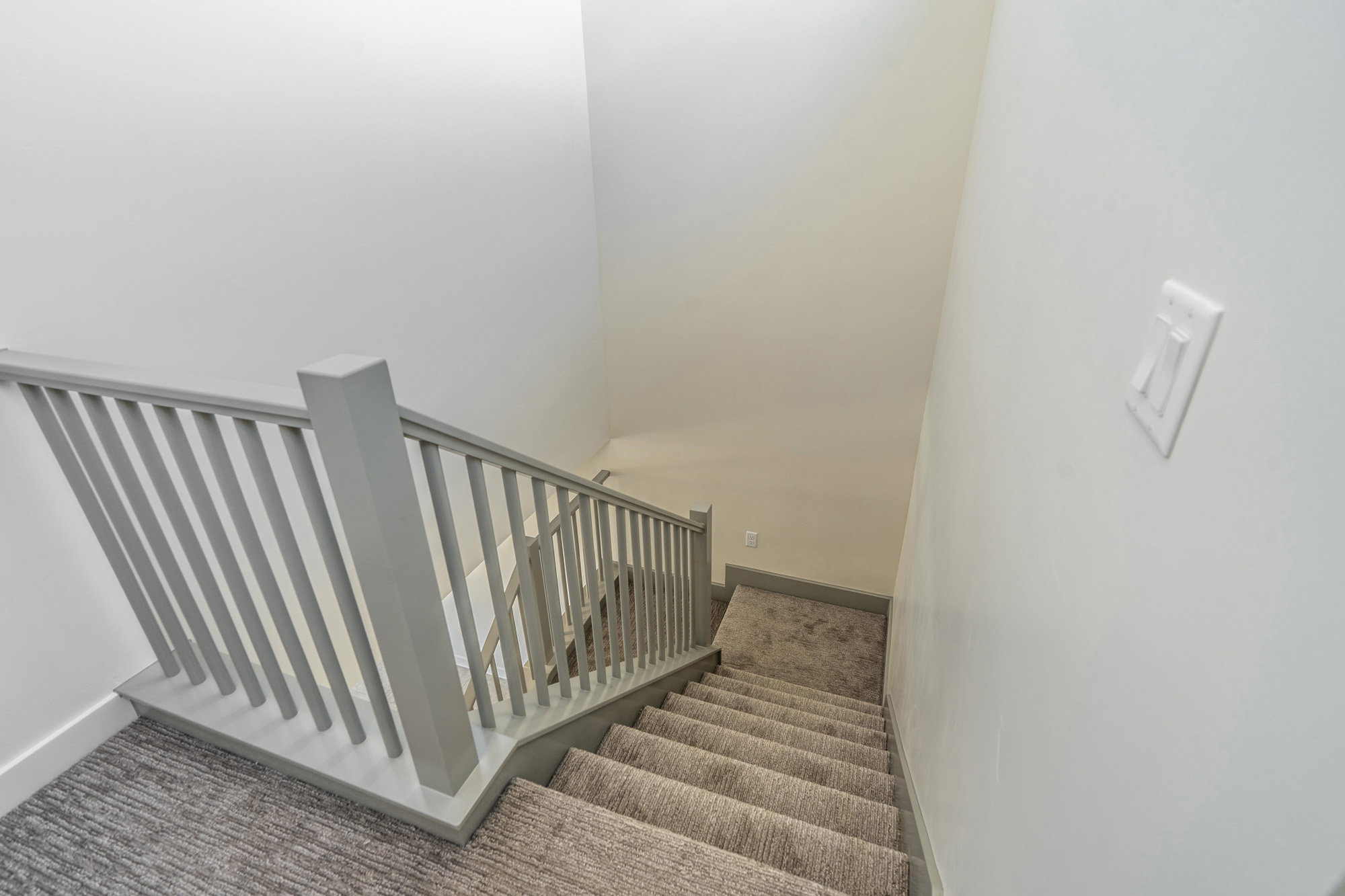 Staircase featuring light gray balusters, white baseboards, and textured carpet flooring