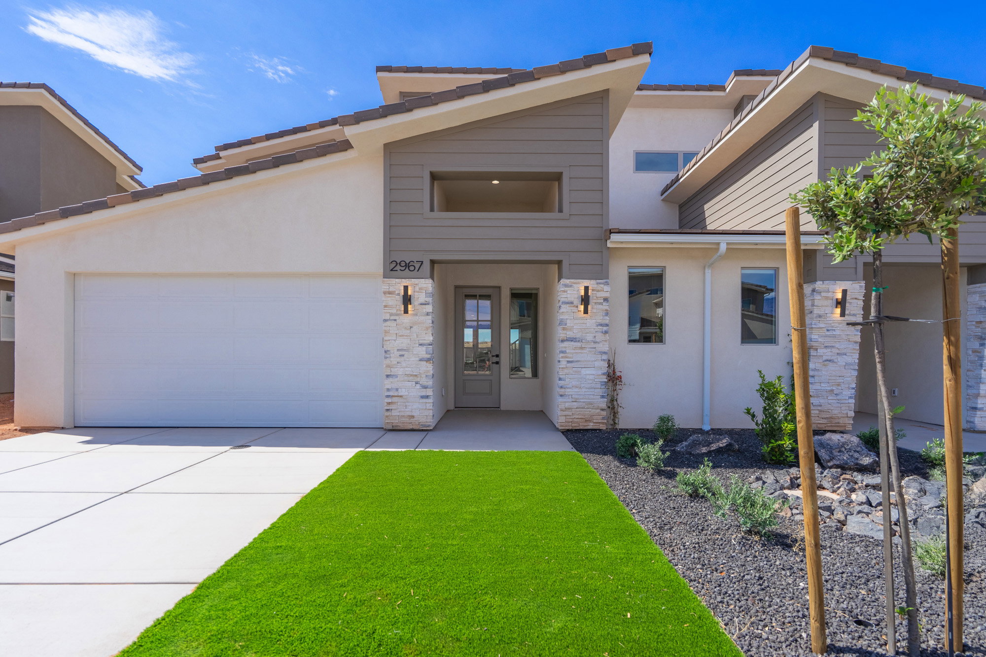 Modern architectural facade featuring stucco and horizontal siding, stone accents, and a distinctive multi-level roofline
