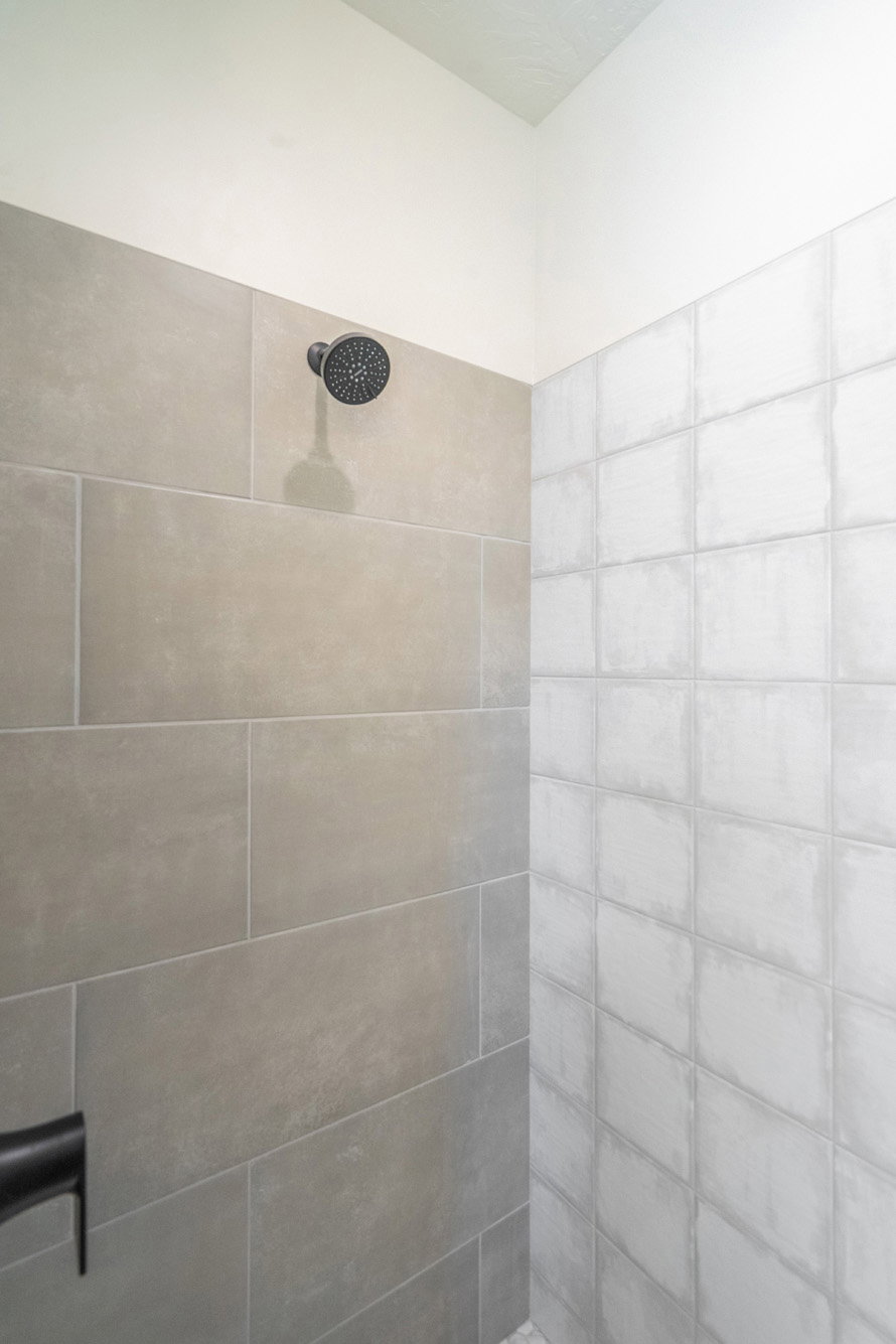 Shower enclosure featuring large format grey wall tiles, textured white square tiles, and a matte black shower head