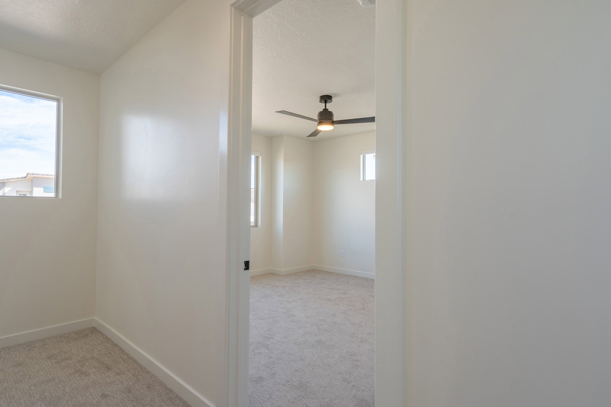 Interior room featuring light-colored carpeting, white wall finishes, and a window providing natural illumination