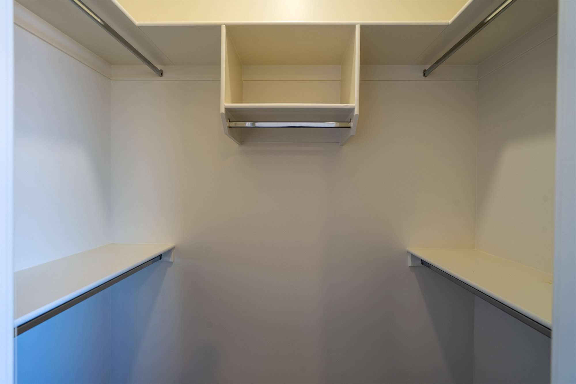 Walk-in closet featuring built-in shelving, multiple hanging rods, and an overhead storage compartment
