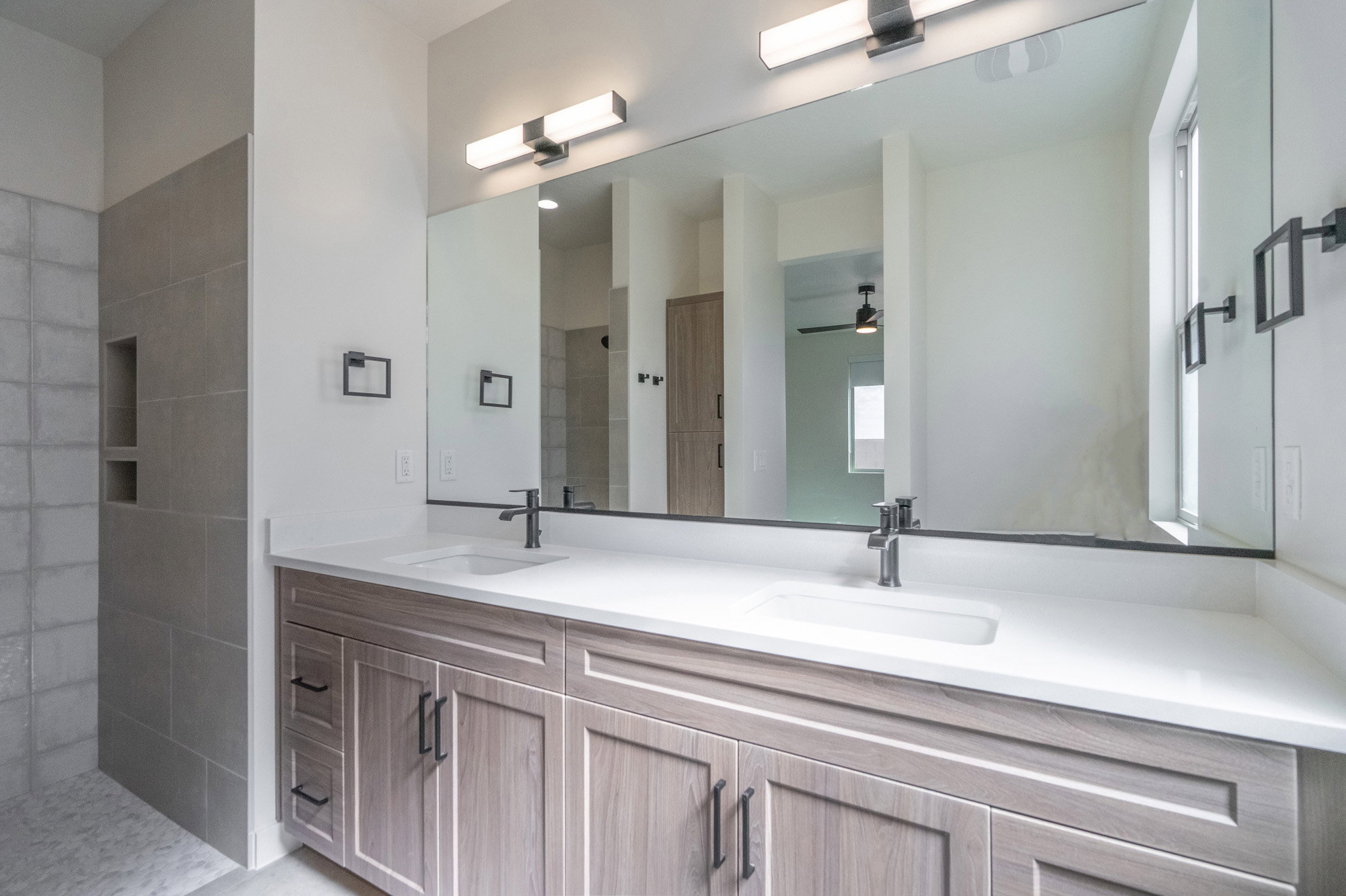 Dual vanity featuring wood-finish cabinetry, white countertops, and matte black fixtures