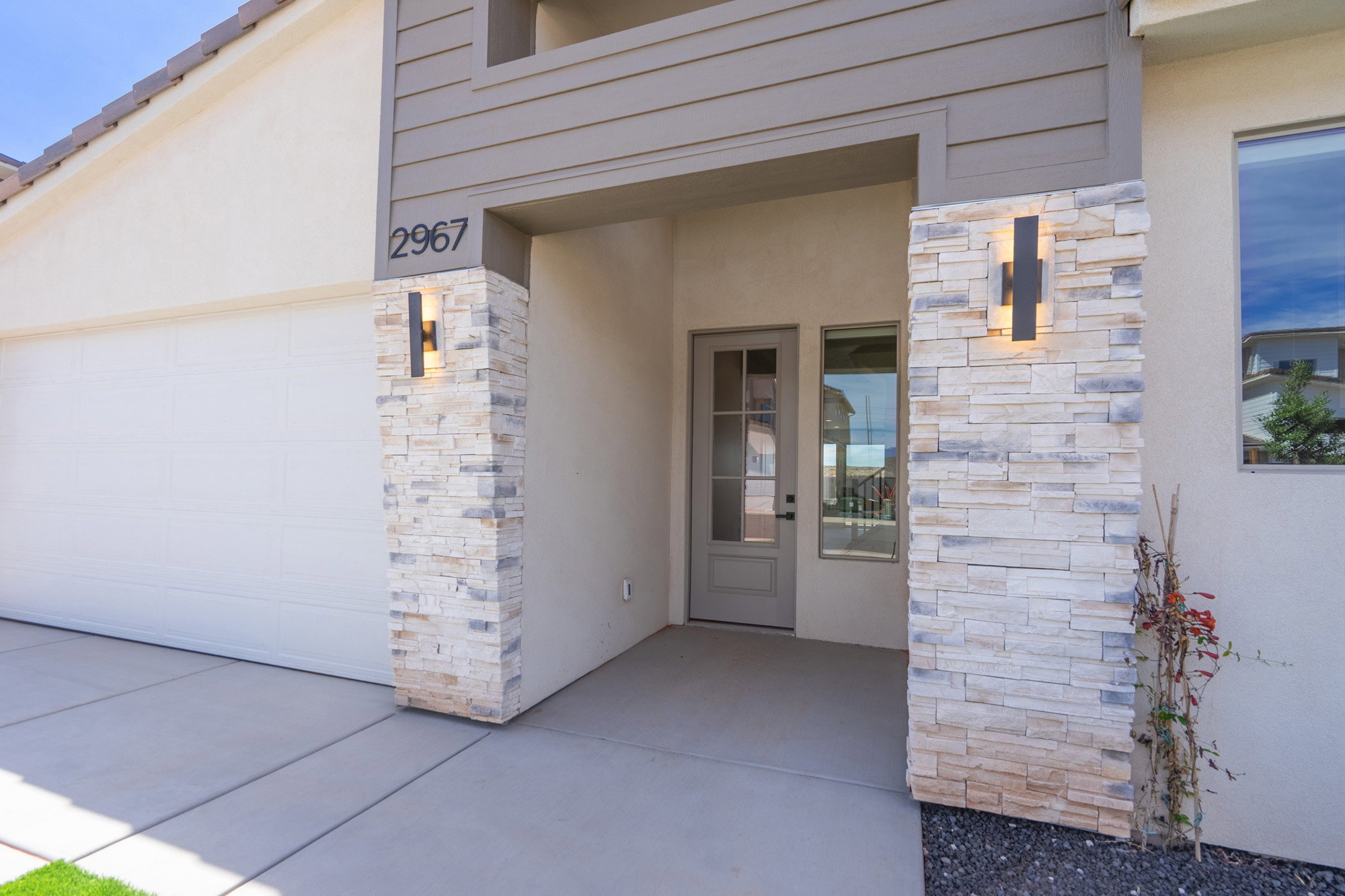Modern exterior featuring stacked stone accents, a paneled garage door, and a recessed entry with contemporary lighting