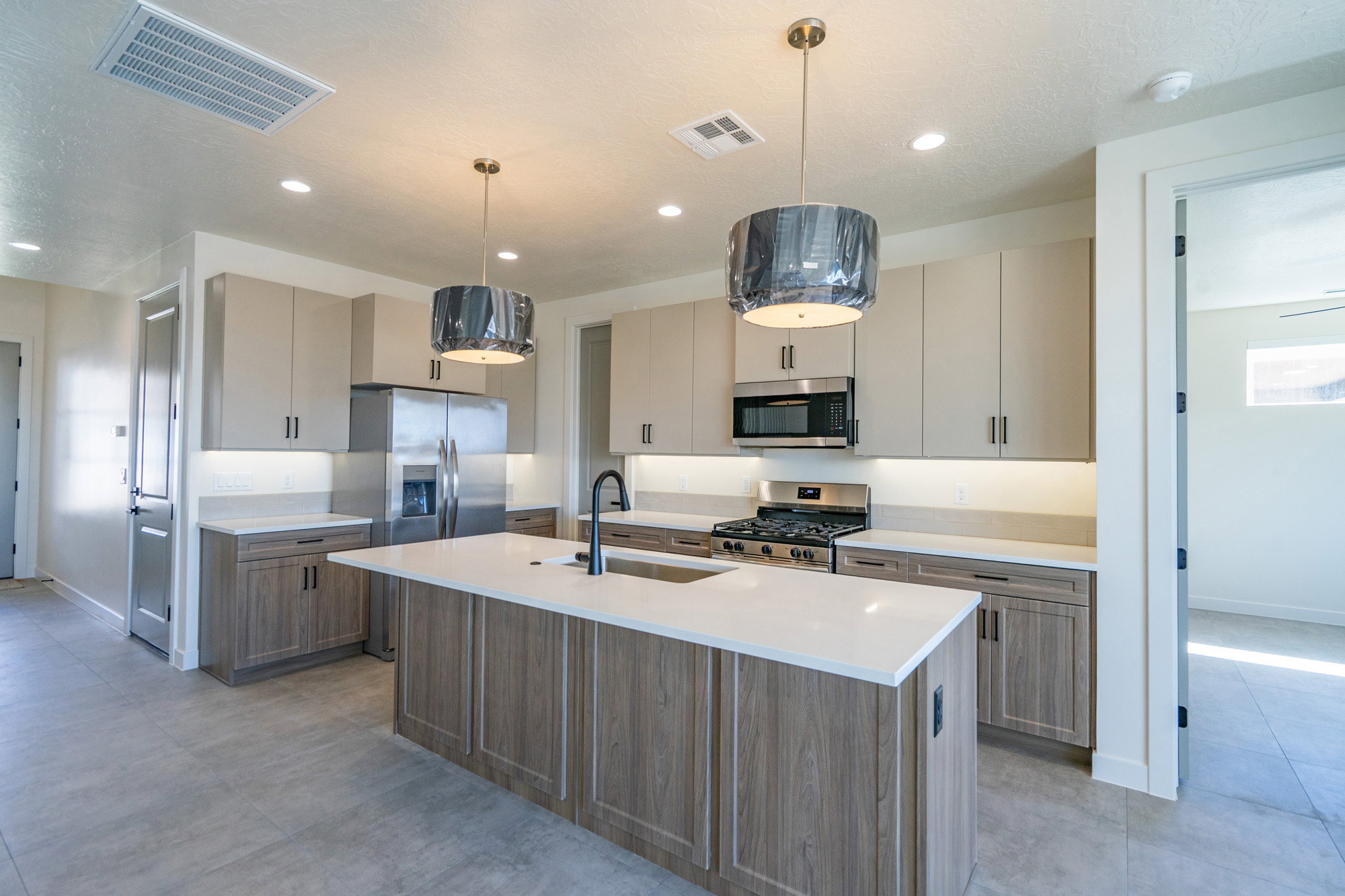 Contemporary kitchen featuring a large central island with a solid surface countertop, stainless steel appliances, two-tone cabinetry, and recessed lighting