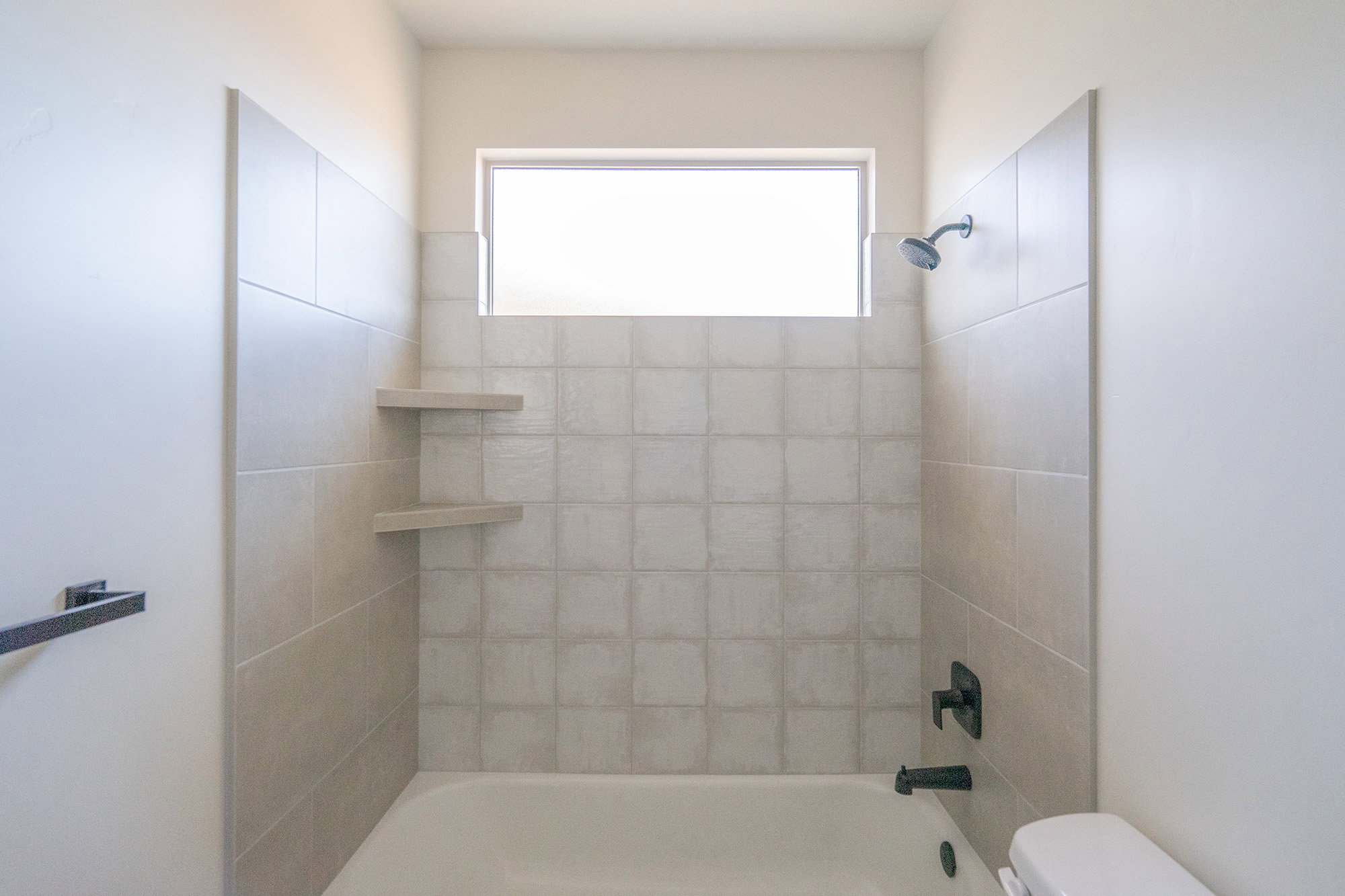 Bathroom featuring a white bathtub, light-toned wall tiling, and a transom window
