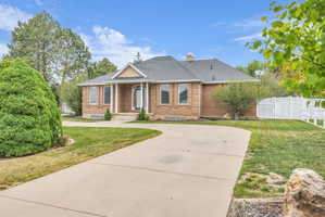 Brick exterior with a prominent portico entry, large front windows, a dark shingle roof, a concrete driveway, and a white fence