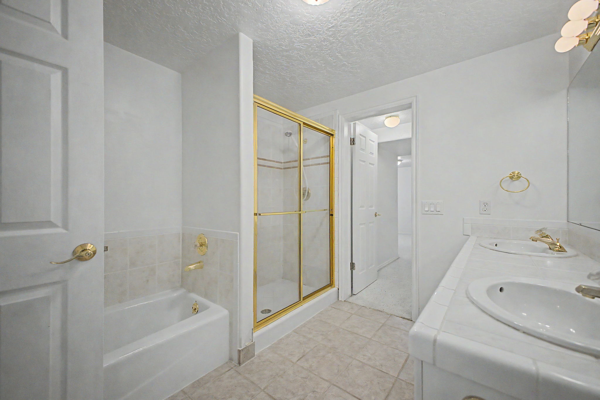 Bathroom featuring a dual vanity, gold-framed glass shower enclosure, and a built-in bathtub with tiled surround