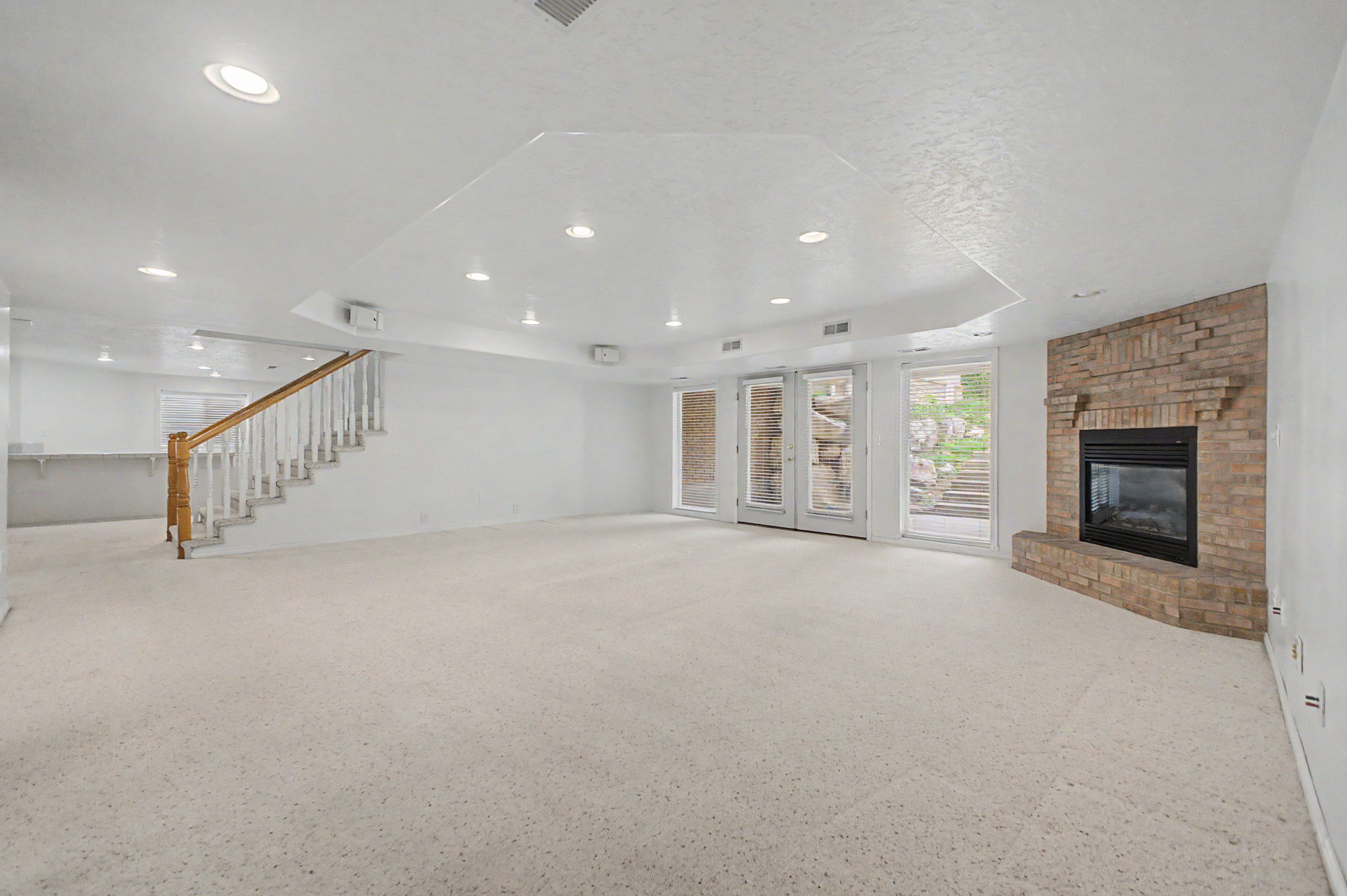 Spacious room featuring light-toned carpeting, a brick fireplace, and double glass doors