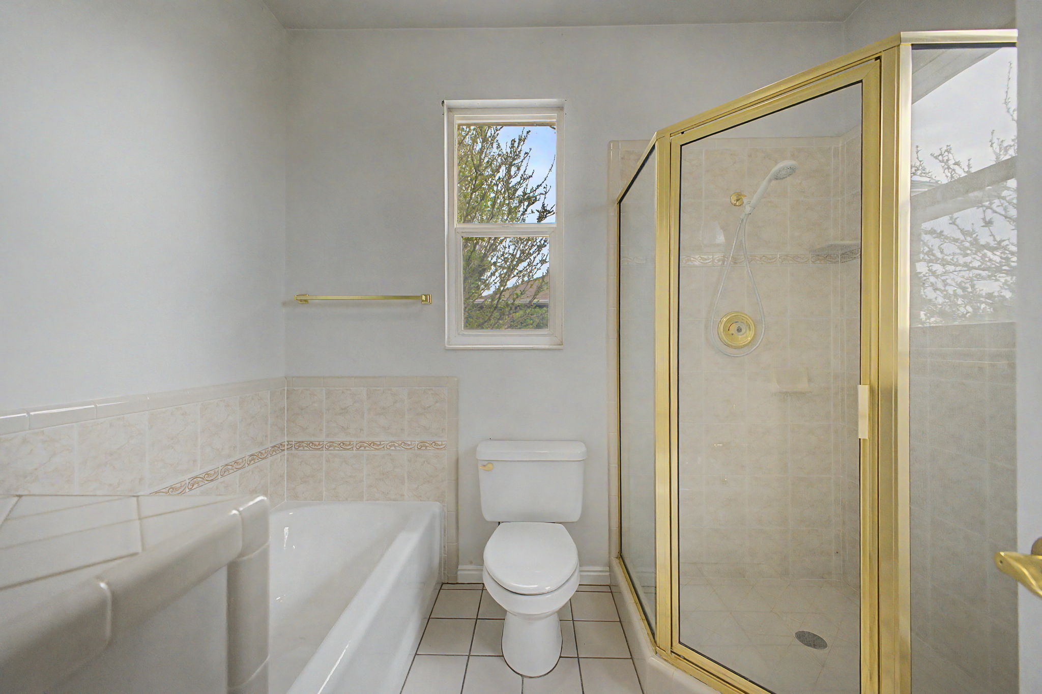 Bathroom featuring a gold-framed glass shower enclosure, a built-in bathtub, and a window
