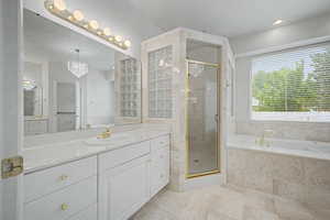 Bathroom featuring a double vanity with white cabinetry, a built-in tub, a glass-enclosed shower, and a large window