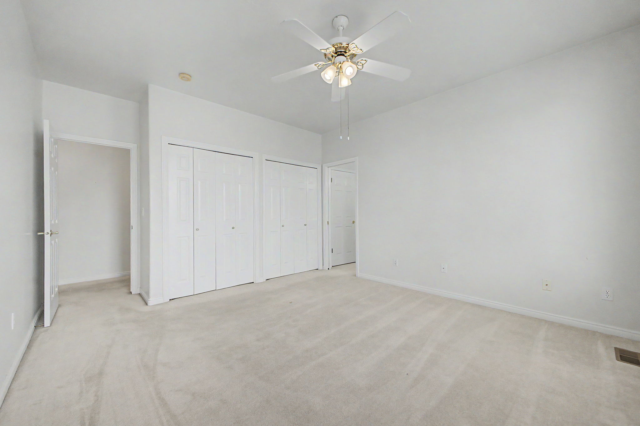 Spacious room featuring neutral carpeting, a ceiling fan with integrated lighting, and multiple bi-fold closet doors