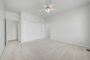 Spacious room featuring neutral carpeting, a ceiling fan with integrated lighting, and multiple bi-fold closet doors