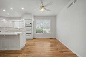 Kitchen and dining area featuring wood-finish flooring, white cabinetry, built-in double ovens, and a tile countertop