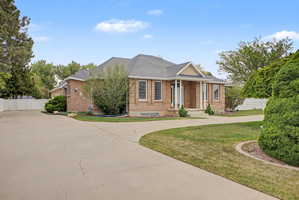 Brick exterior residence featuring a covered entry porch with white columns, a curved driveway, and a shingled roof