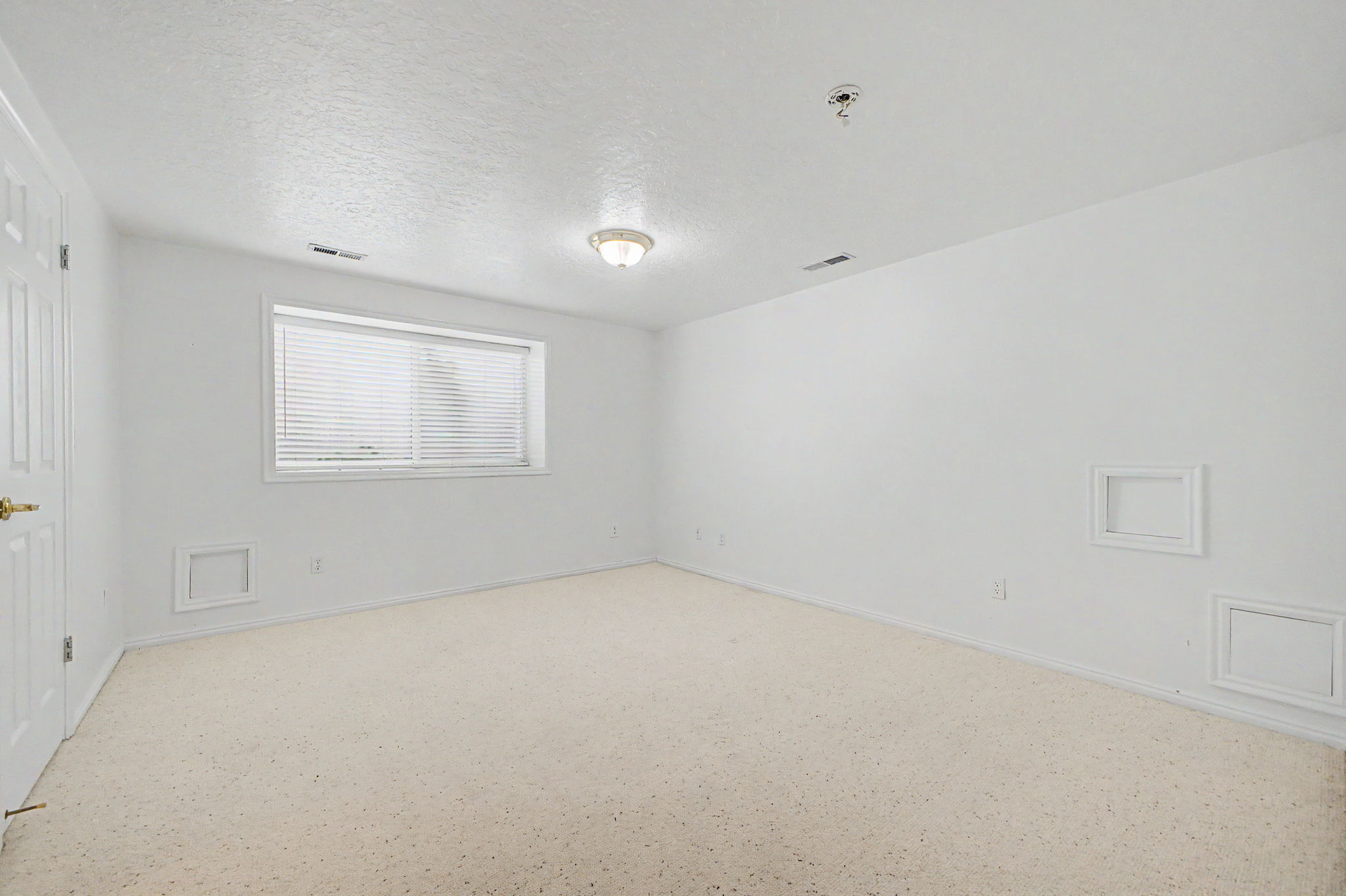 Spacious room featuring neutral carpeting, white walls, and a window with horizontal blinds
