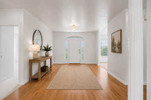 Virtually Staged-Bright entryway featuring wood-finish flooring, a decorative front door with arched transom, and a frosted glass chandelier