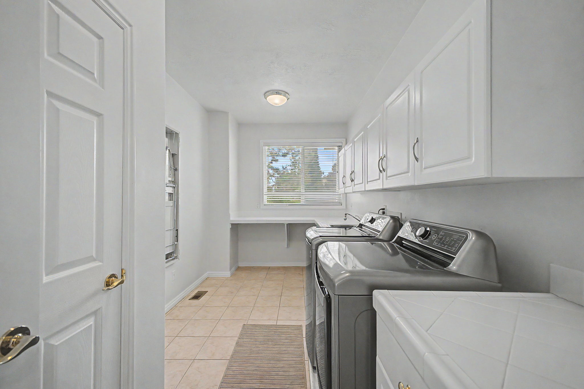 Dedicated laundry room featuring tile flooring, white shaker-style cabinetry, and a countertop workspace