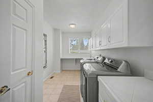 Dedicated laundry room featuring tile flooring, white shaker-style cabinetry, and a countertop workspace