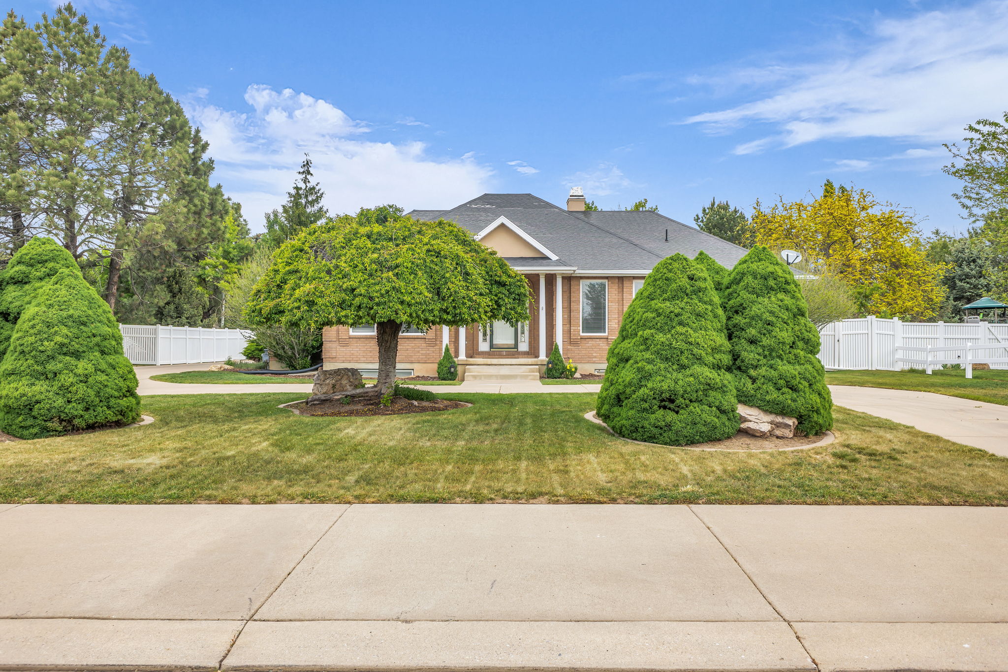 Brick-front residence featuring a covered entry, mature landscaping, and an expansive concrete driveway