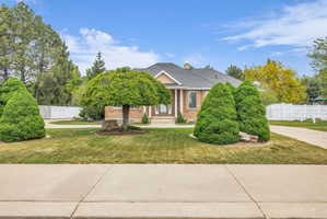 Brick-front residence featuring a covered entry, mature landscaping, and an expansive concrete driveway