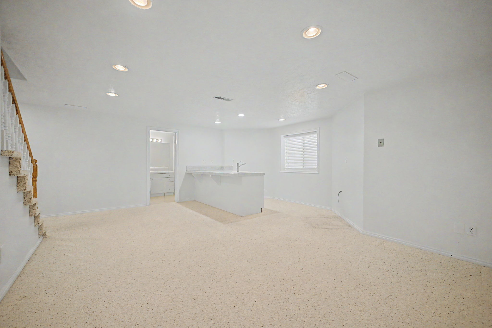 Spacious room featuring light-colored carpeting, recessed lighting, and a built-in wet bar with a sink and countertop