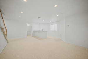 Spacious room featuring light-colored carpeting, recessed lighting, and a built-in wet bar with a sink and countertop