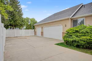 Expansive concrete driveway with a two-car garage featuring individual white doors and brick accents