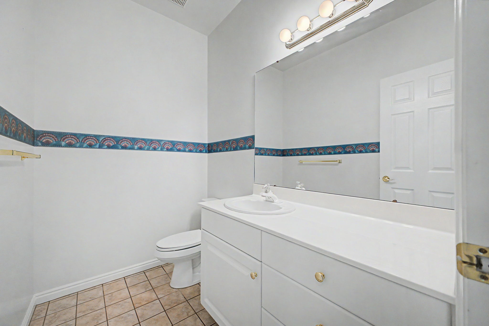 White vanity with integrated sink, brushed nickel lighting fixture, large wall-mounted mirror, and neutral tiled flooring