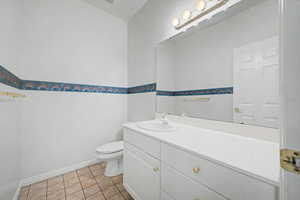 White vanity with integrated sink, brushed nickel lighting fixture, large wall-mounted mirror, and neutral tiled flooring