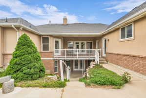 Multi-level exterior featuring stucco and brick finishes, a covered second-story balcony with white railings, and a lower-level patio with double glass doors