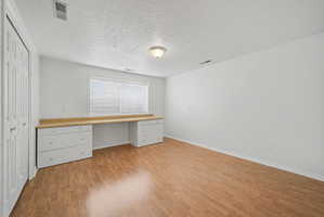 Room featuring wood-finish flooring, a built-in desk with a light wood-finish countertop, white cabinetry with gold-tone hardware, and a window with horizontal blinds
