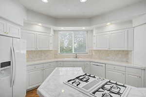Kitchen featuring white cabinetry with gold-toned hardware, a tile countertop, and a built-in gas range on the island