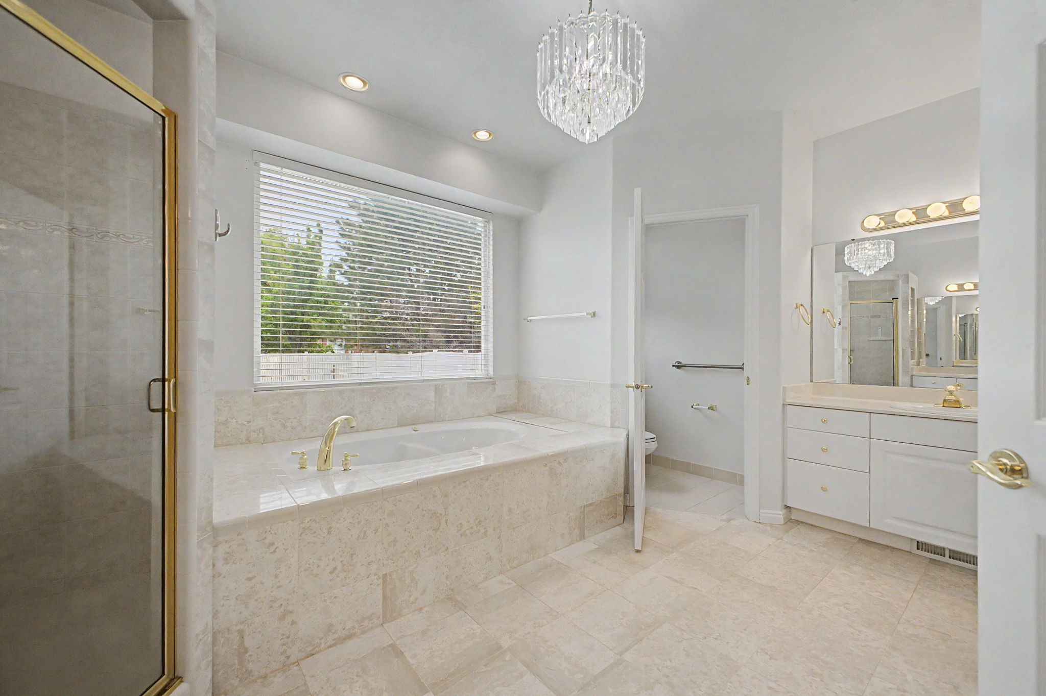 Spacious bathroom featuring a built-in soaking tub with gold-finish fixtures, a separate glass-enclosed shower with gold-finish trim, and a double vanity with a large mirror
