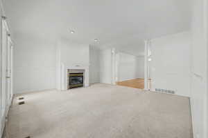 Carpeted room featuring a fireplace with a decorative white mantel, a stone surround, and a glass-front insert