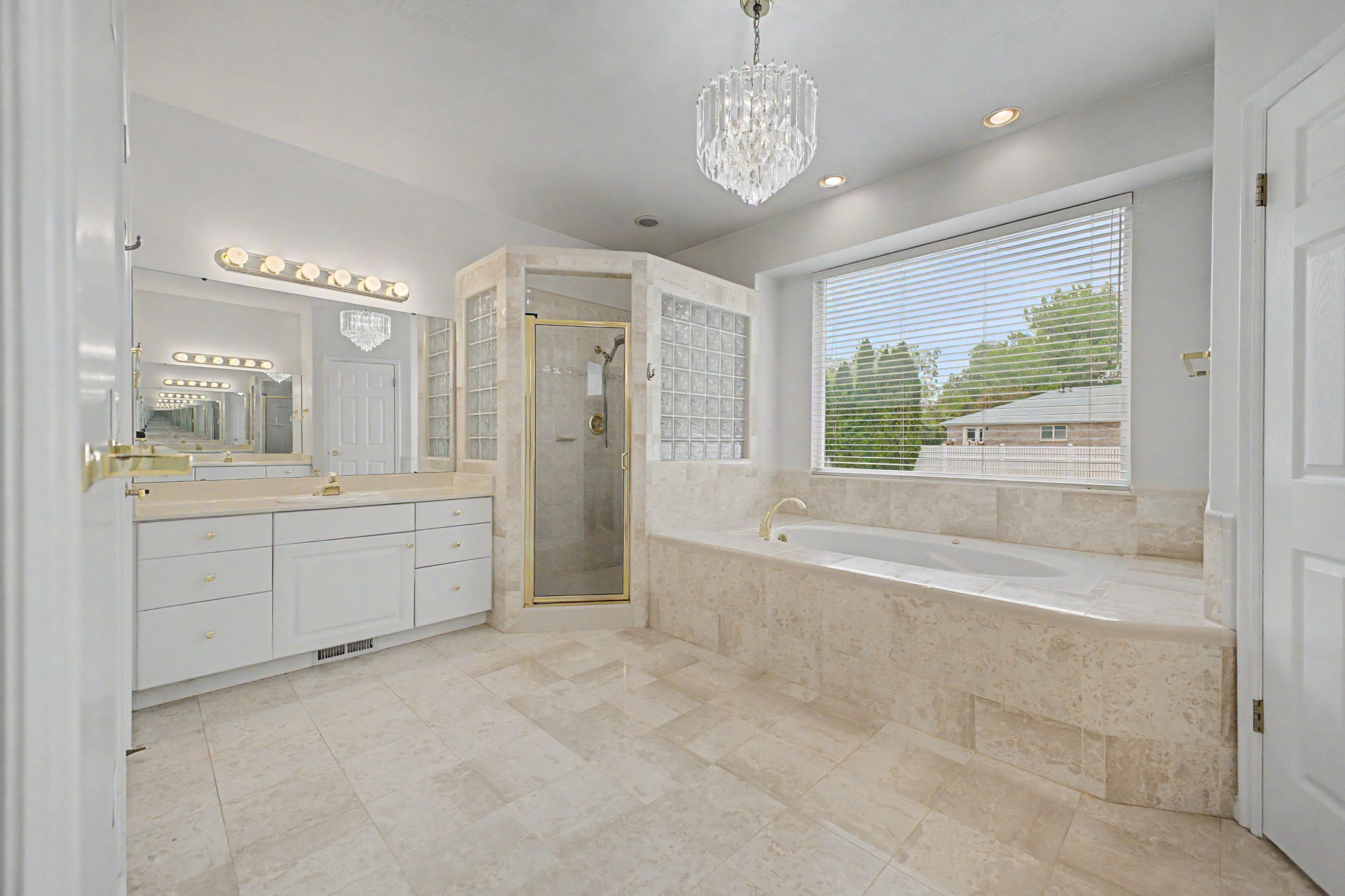Spacious bathroom featuring a large soaking tub with a tiled surround, a separate glass-enclosed shower, dual vanity with white cabinetry, and recessed lighting