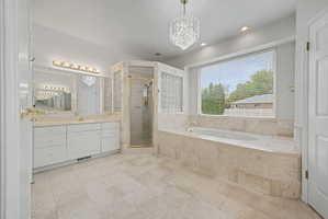 Spacious bathroom featuring a large soaking tub with a tiled surround, a separate glass-enclosed shower, dual vanity with white cabinetry, and recessed lighting