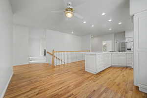Kitchen and living area featuring wood-finish flooring, white cabinetry, a central island, and recessed lighting