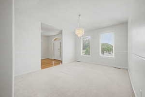 Carpeted room featuring a tiered crystal chandelier, two windows with blinds, and white wall paneling