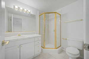 Bathroom featuring a corner shower with a gold-finish frame, a vanity with a tiled countertop and integrated sink, white cabinetry with gold-tone hardware, and a large wall-mounted mirror with overhead lighting