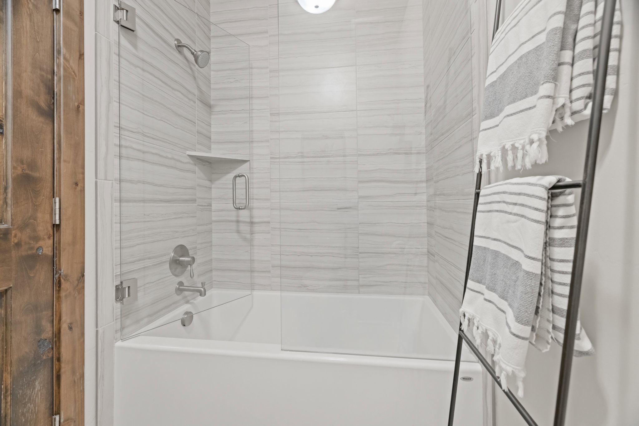 Full bath featuring a white tub, glass shower enclosure, and a tiled shower surround with an integrated corner shelf