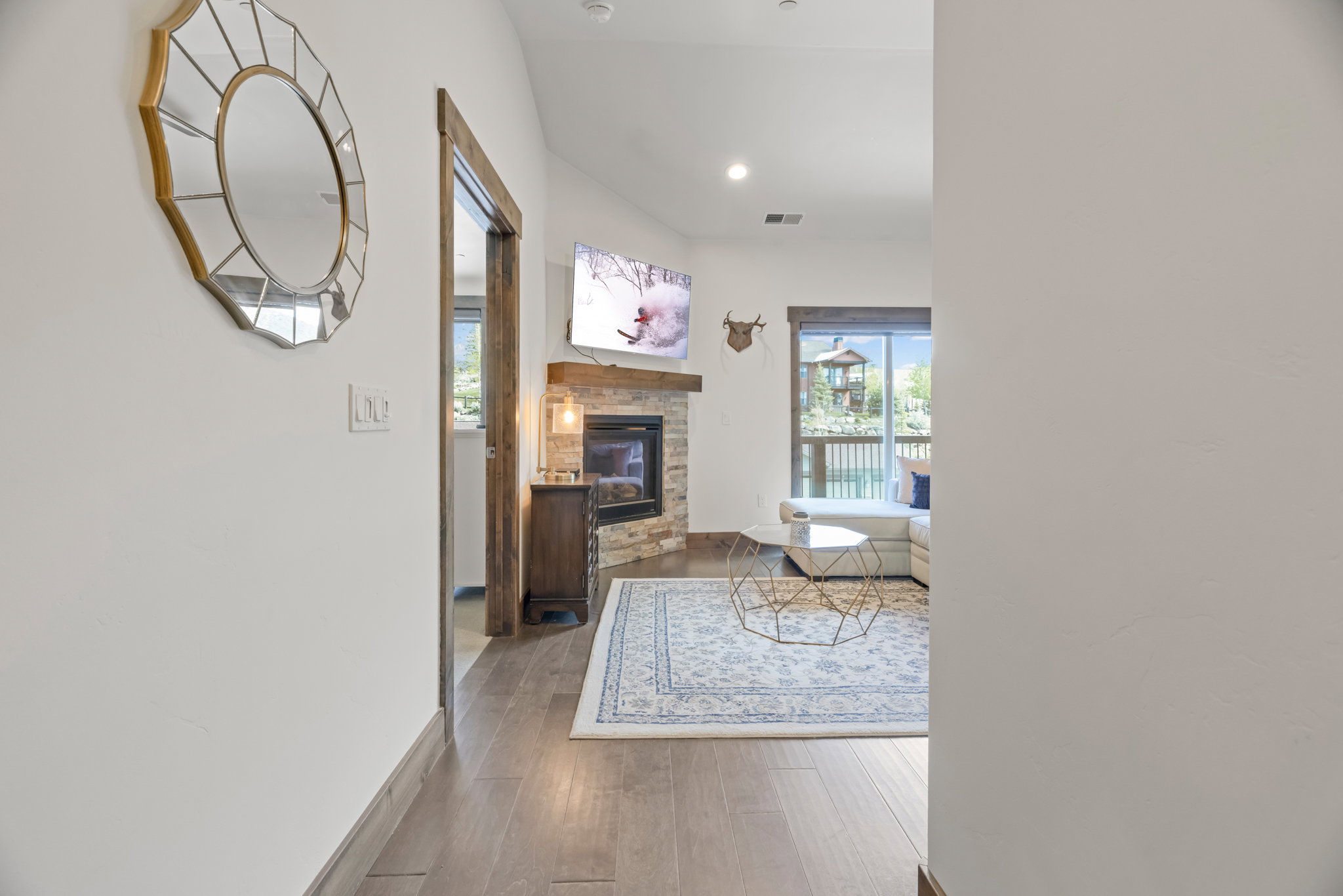 Living area featuring wood-finish flooring, a stone-faced fireplace with a wood mantel, and an exposed wood door frame