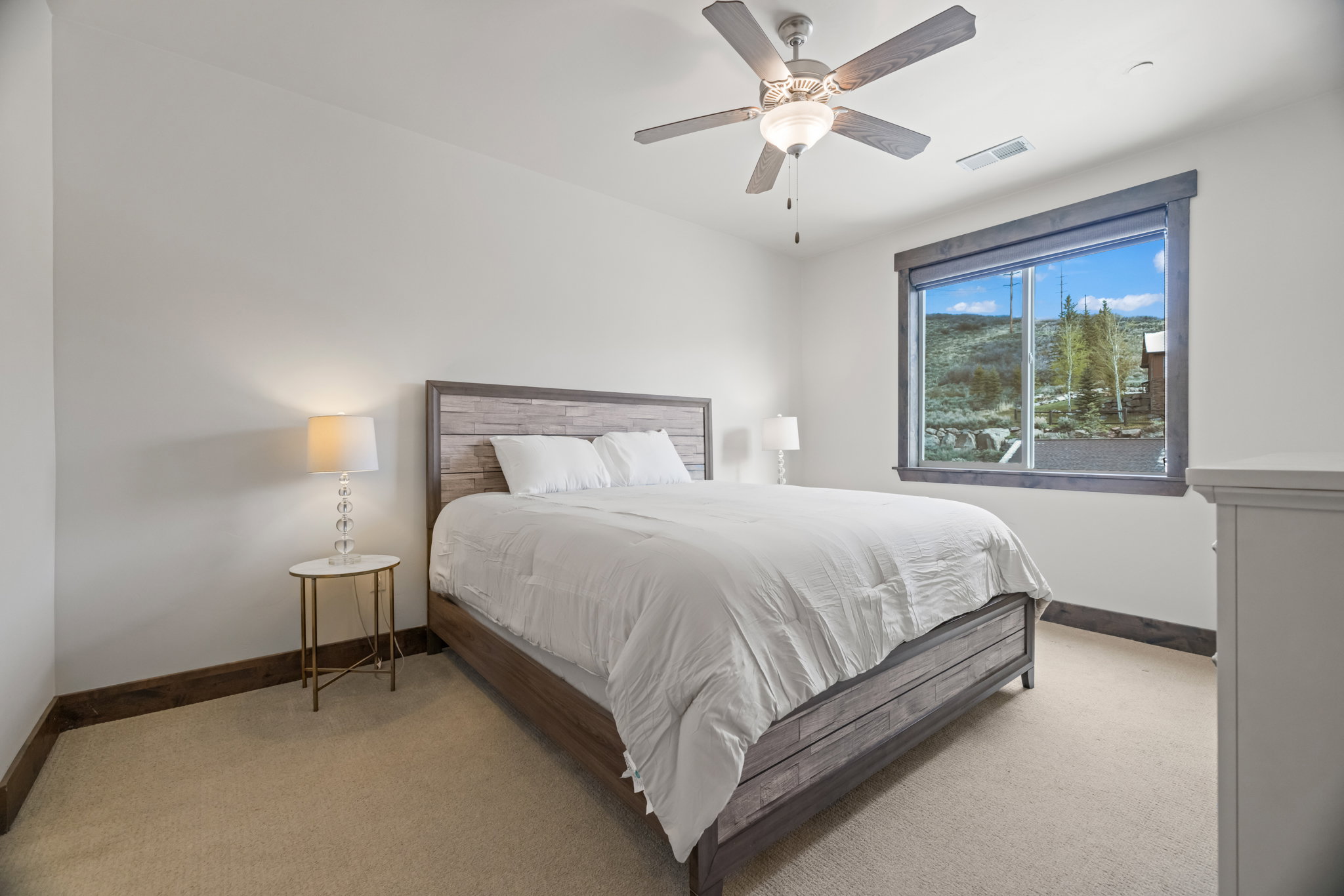 Bedroom featuring a large window with mountain scenery, a ceiling fan with integrated lighting, wood-finish baseboards, and neutral carpeting